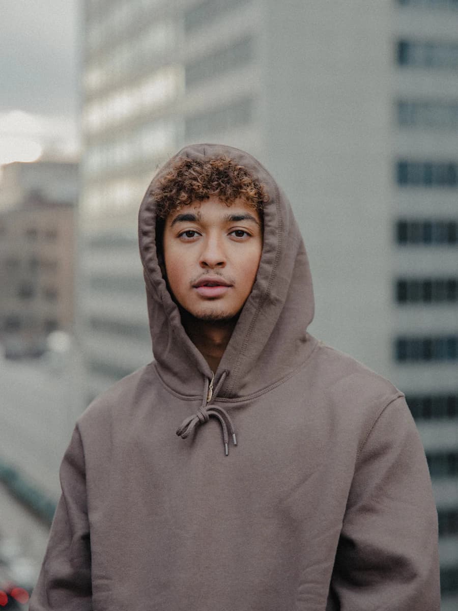 Adult model style reference — man in gray hoodie standing in front of white building during daytime