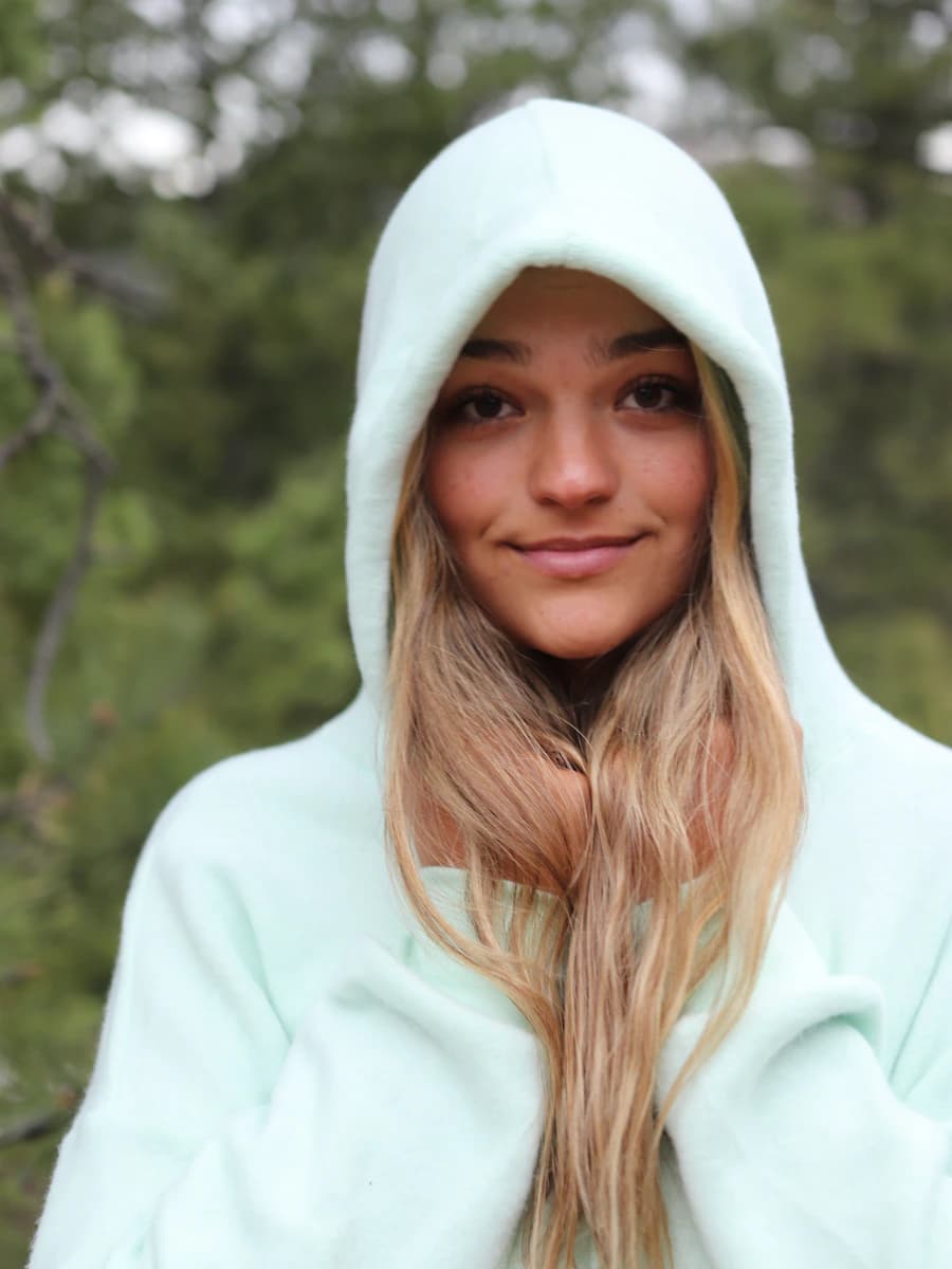 Adult model style reference — woman in white hoodie standing near green trees during daytime